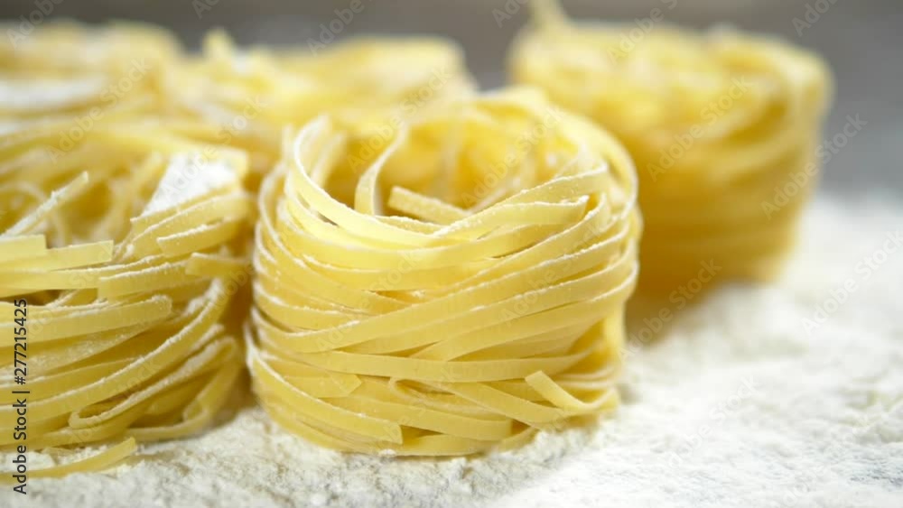 Fettuccine, raw pasta, closeup lie in white flour on a wooden table Fettuccine, raw pasta, closeup lie in white flour on a wooden table