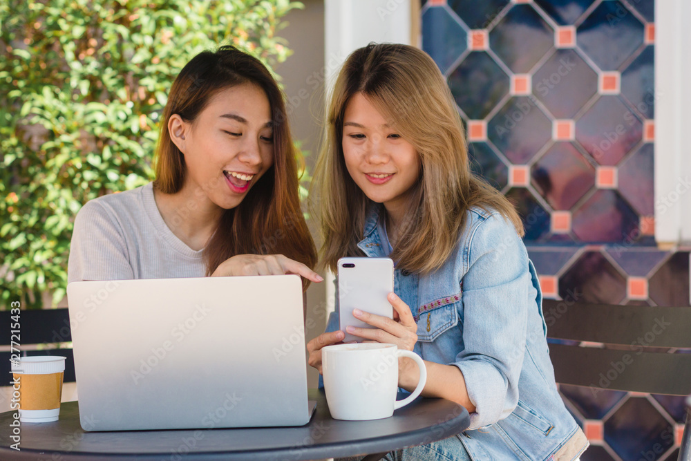 Asian young women working on laptop using and looking smartphone and drinking coffee while sitting in cafe. Lifestyle women communication and working in coffee shop concept. Asian young women working on laptop using and looking smartphone and drinking coffee while sitting in cafe. Lifestyle women communication and working in coffee shop concept.
