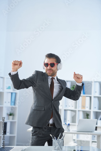 Happy man in formalwear, sunglasses and headphones dancing by workplace
