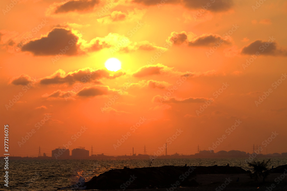 Conceptual of hot industrial estate on another side of sea, cloudy red sky and shining sun