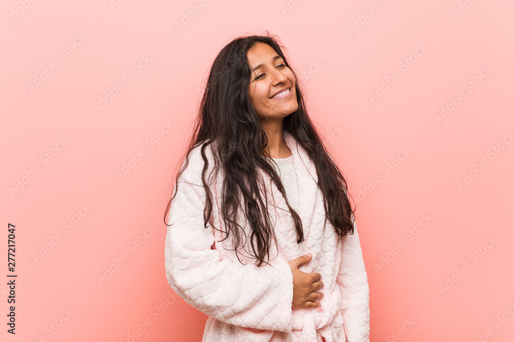 Young indian woman wearing pajama touches tummy, smiles gently, eating and satisfaction concept.