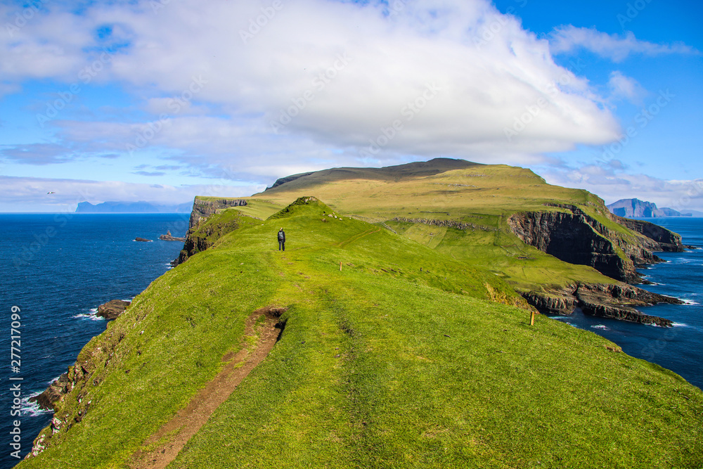 Female hiker among the green landscape of Mykines Island in the Faroes