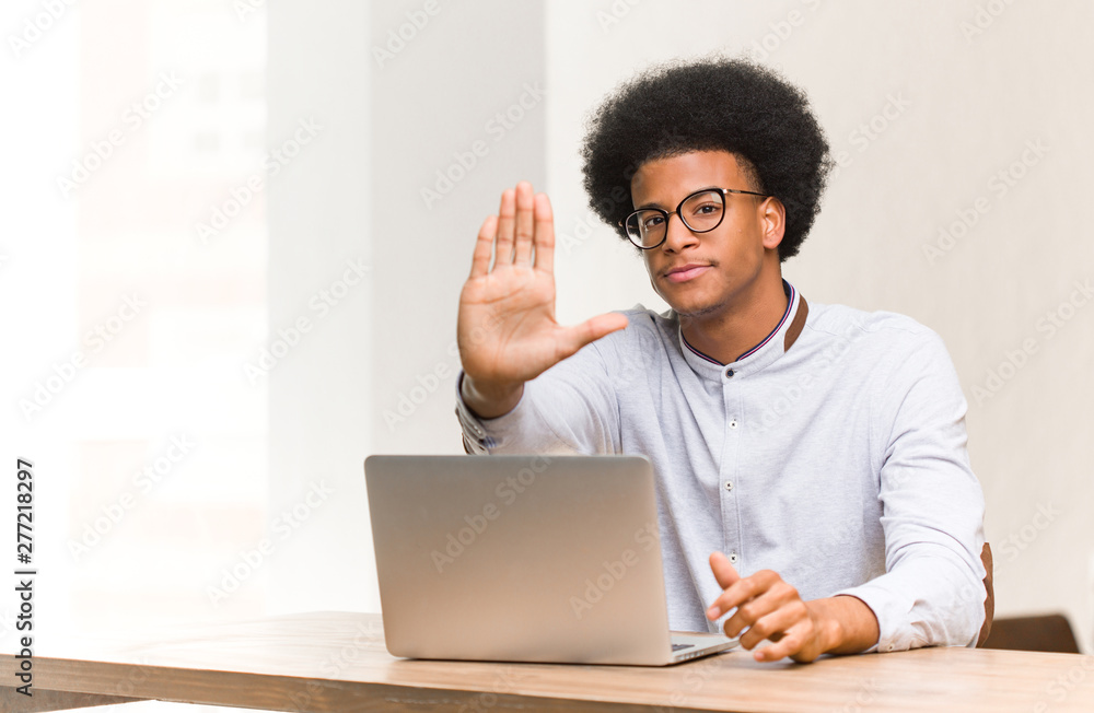 Young black man using his laptop putting hand in front Young black man using his laptop putting hand in front
