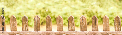 Wooden fence gate pattern with blurred green nature background. Repeating porch wood planks in bright sunny day.