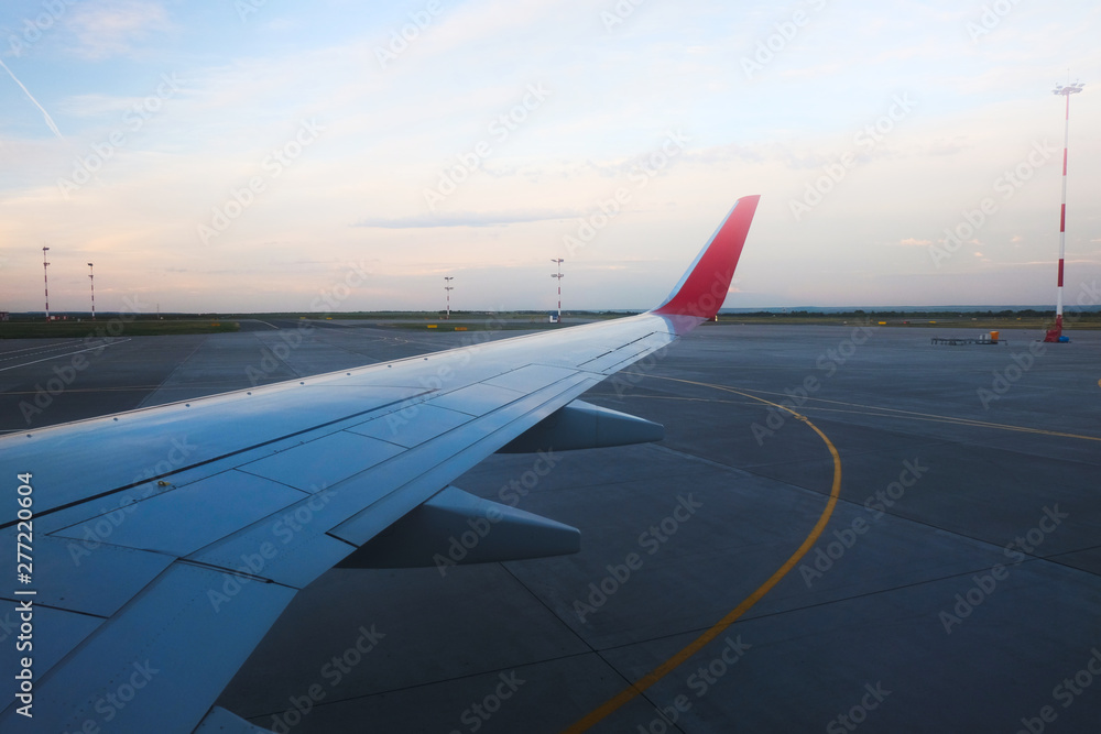 View from the porthole - Wing of an airplane taking off above the runway at high speed during the sunset. The land is running under the wing