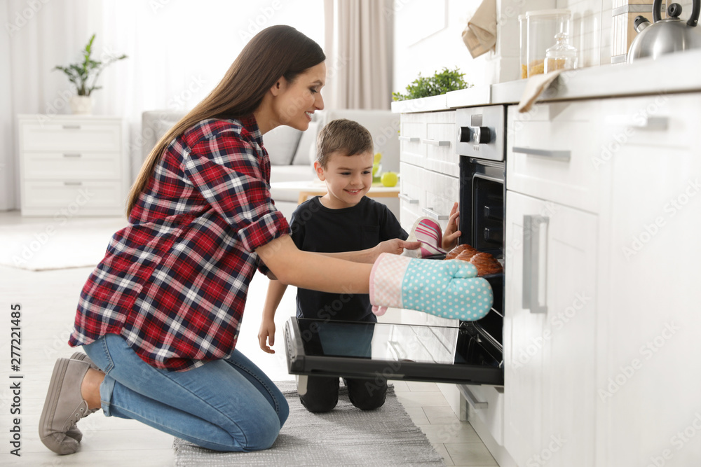 Son and mother taking out tray of baked buns from oven in kitchen Son and mother taking out tray of baked buns from oven in kitchen