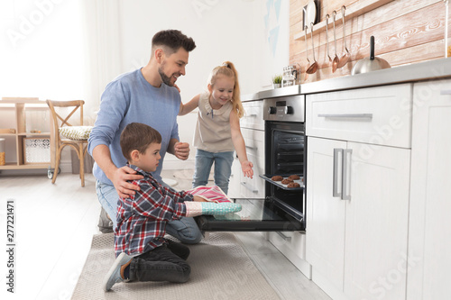 Father with his kids baking cookies in oven at home
