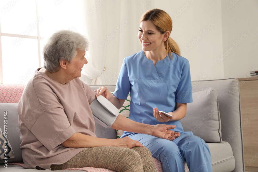 Obraz premium Nurse measuring blood pressure of elderly woman indoors. Assisting senior people