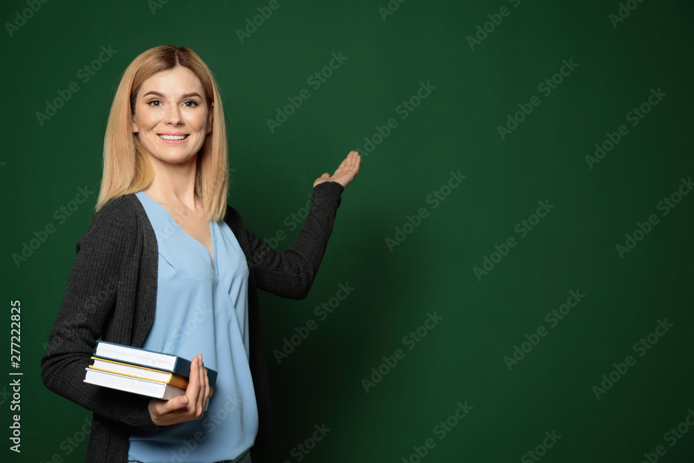 Beautiful teacher with books pointing at chalkboard, space for text Beautiful teacher with books pointing at chalkboard, space for text
