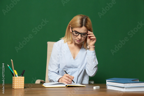 Portrait of beautiful teacher sitting at table near chalkboard