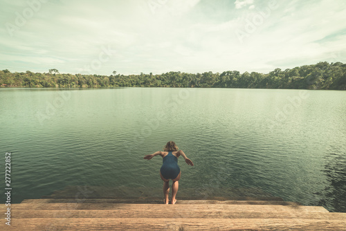 Obraz na płótnie Woman jumping into the water of volcanic lake surrounded by forest in Banlung, Cambodia, travel destination. Toned vintage style w salonie