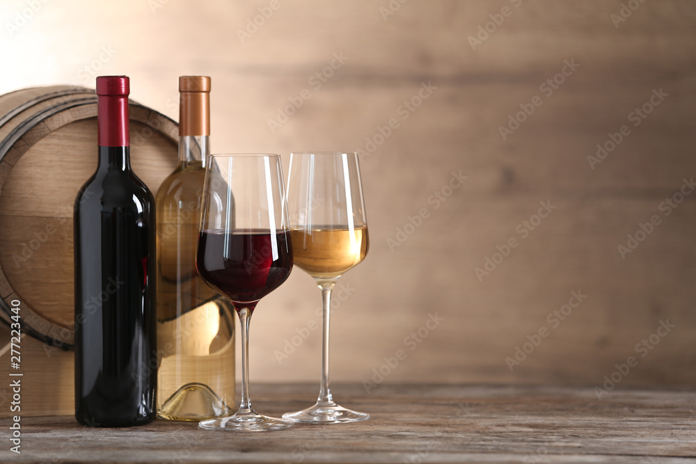 Glasses and bottles of different wine near wooden barrel on table. Space for text