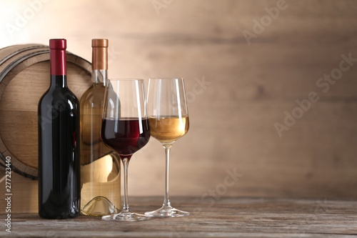 Foto Glasses and bottles of different wine near wooden barrel on table