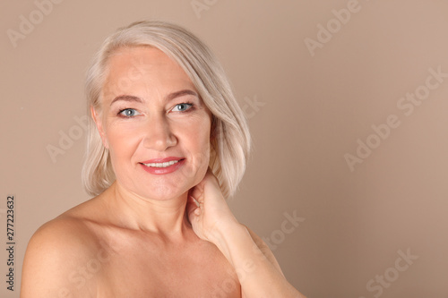 Portrait of charming mature woman with healthy beautiful face skin and natural makeup on beige background  space for text
