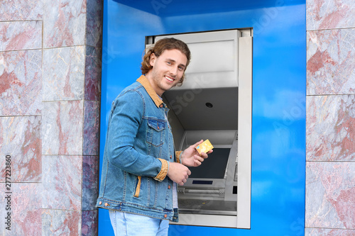 Young man with credit card near cash machine outdoors