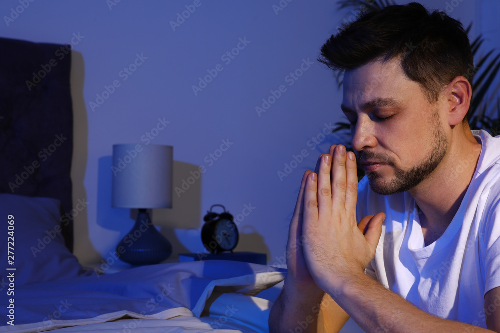 Fototapeta premium Handsome man saying bedtime prayer in dark room at night. Space for text