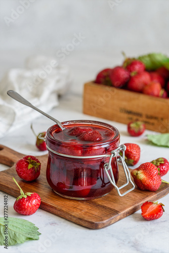 A jar of strawberry jam on a wooden board on a marble background 