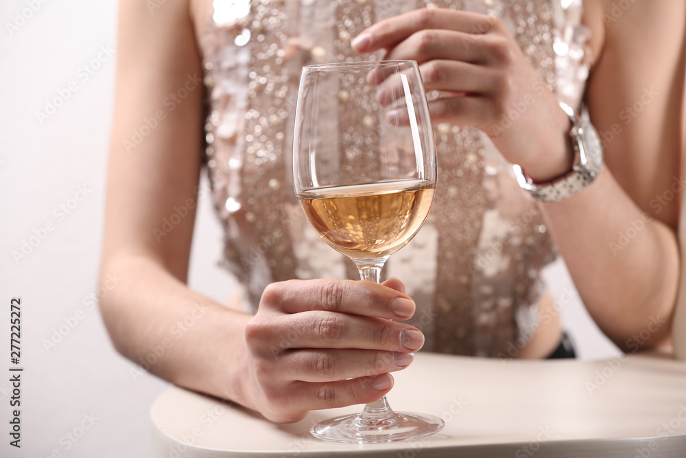 Woman in dress holding glass of white wine at table, closeup
