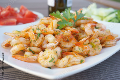 fried shrimps on a white plate with herbs, tomatoes, cucumbers, bottle of wine