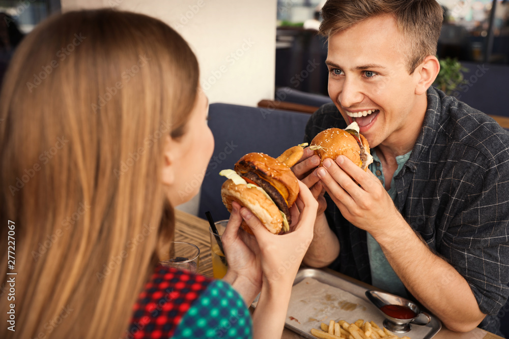 Young couple eating burgers in street cafe Young couple eating burgers in street cafe