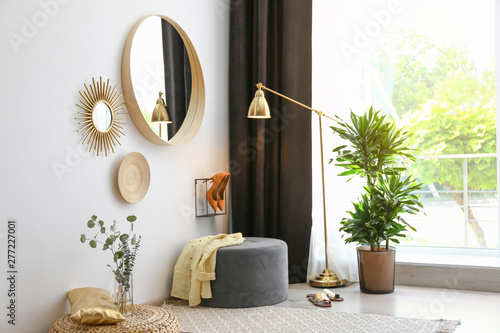 Hallway interior with big round mirror and ottoman chair near white wall