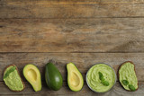 Flat lay composition with guacamole, sandwiches and avocados on wooden table. Space for text