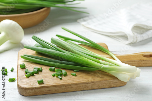Wooden board with cut fresh green onions on white table