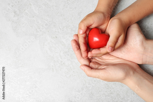 Woman and child holding heart on grey stone background, top view with space for text. Donation concept