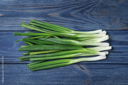 Fresh green onions on blue wooden background, top view