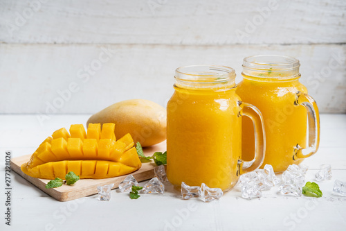 Refreshing mango smoothies in glass with ripe mango on white wooden table