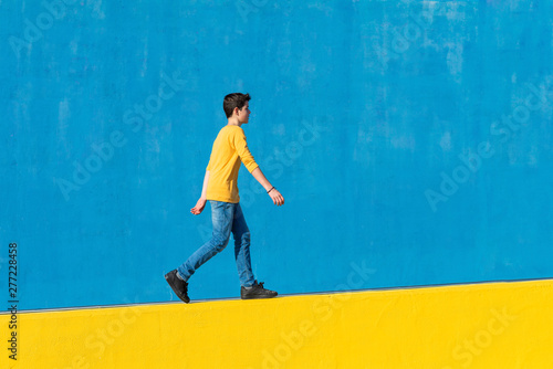 Young boy wearing casual clothes walking against a blue wall