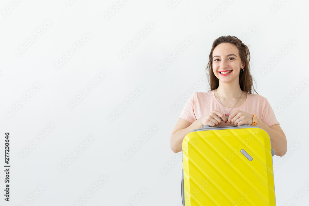 Portrait of a beautiful young brunette woman with a yellow suitcase in her hands posing at a white background with copy space. Travel and tourism concept. Portrait of a beautiful young brunette woman with a yellow suitcase in her hands posing at a white background with copy space. Travel and tourism concept.