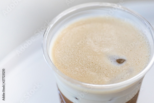 Close up of milk foam of iced coffee latte in take away plastic cup on white table.