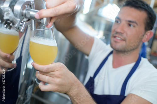 worker in brewery pouring glass of beer from vat