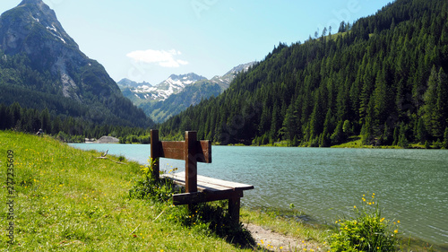 Empty Wodden Bench in front of lake Schliereralmsee with mountain scenery in Radstaedter Tauern, Niedere Tauern, Austrian Alps, Austria, June 2019 photo