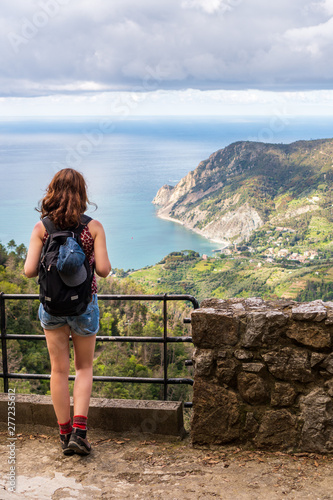 Young tourist woman hiker enjoying the wonderful panoramic view from the Soviore Sanctuary over the Ligurian Sea and Monterosso village, in Cinque Terre, Italy. Hiking on a summer day. 