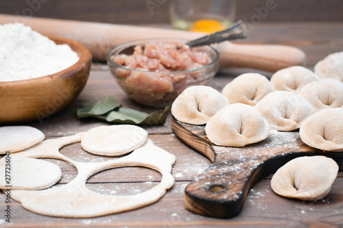 Raw dumplings on the cutting board and ingredients for their preparation: flour, egg, minced meat on a wooden table