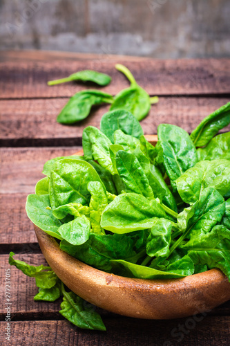 Fresh baby spinach leaves in a bowl on a wooden table. Rustic style