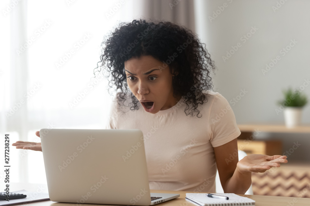 Shocked angry stressed african woman customer looking at laptop screen Shocked angry stressed african woman customer looking at laptop screen