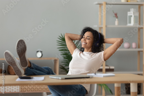 Relaxed african woman wear headphones listening to music at desk