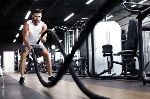 Fototapeta Naklejka Na Ścianę i Meble -  Athletic young man with battle rope doing exercise in functional training fitness gym.
