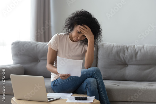 Stressed african woman holding bills worried about bankruptcy bank debt