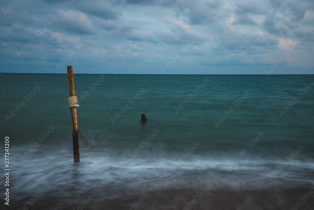 Long exposure of sea water with wooden logs and rope, on cloudy sky