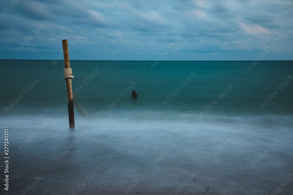 Long exposure of sea water with wooden logs and rope, on cloudy sky Long exposure of sea water with wooden logs and rope, on cloudy sky