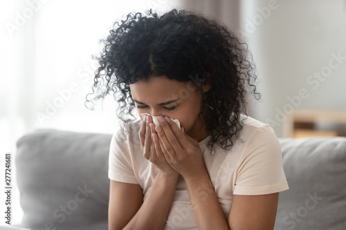 Ill allergic african woman blowing nose in tissue at home photo