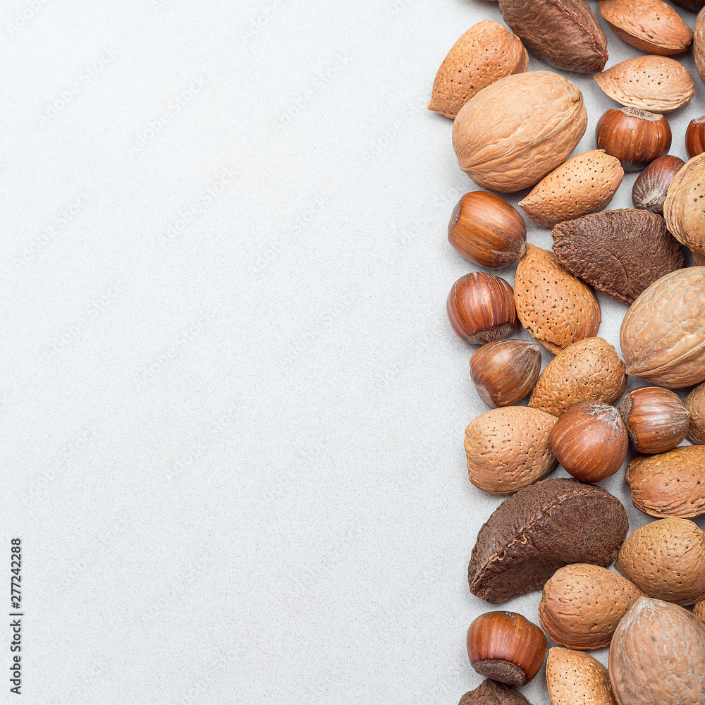 Different kinds of nuts in shell, hazelnut, walnut, almond and brazil nuts on a gray background, square format, top view, copy space Different kinds of nuts in shell, hazelnut, walnut, almond and brazil nuts on a gray background, square format, top view, copy space