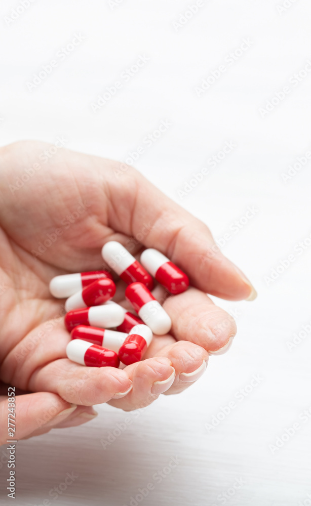 Hand holds red and white pills on a white table background. Concept of medication of vitamins and microelements. Treatment and prevention. Hand holds red and white pills on a white table background. Concept of medication of vitamins and microelements. Treatment and prevention.