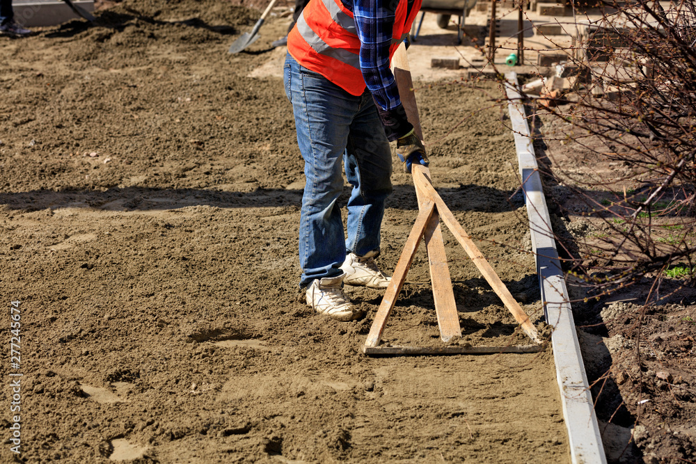 The worker aligns the foundation with a wooden level for laying tiles on the sidewalk. The worker aligns the foundation with a wooden level for laying tiles on the sidewalk.