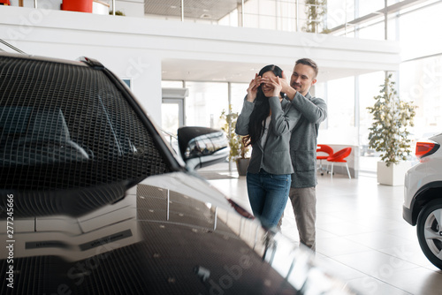 Couple buying car in showroom, surprise for woman