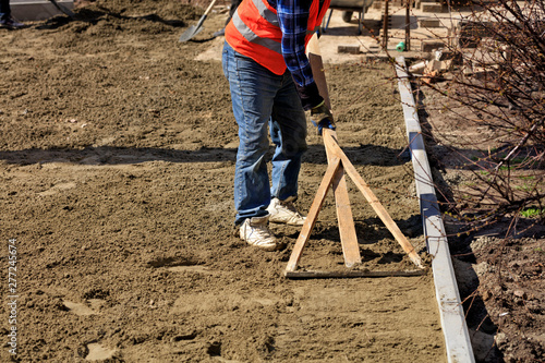 The worker aligns the foundation with a wooden level for laying tiles on the sidewalk.